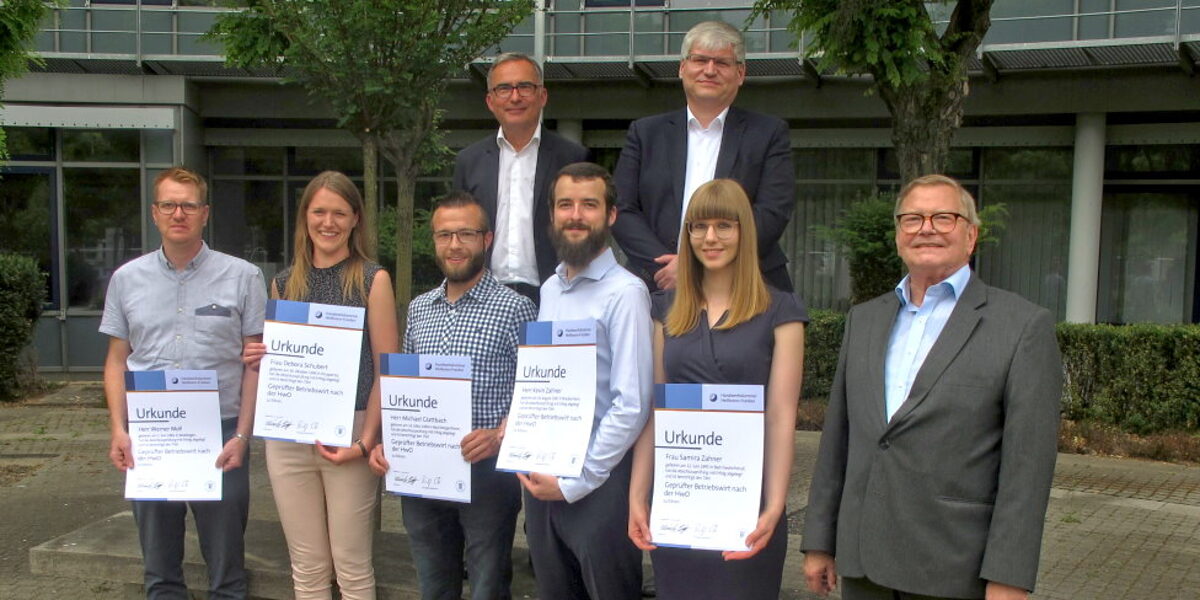 Erfolgreicher Abschluss: die neuen Betriebswirte. Zwei Reihen mit insgesamt acht Personen. Fünf davon halten eine Urkunde in ihren Händen.