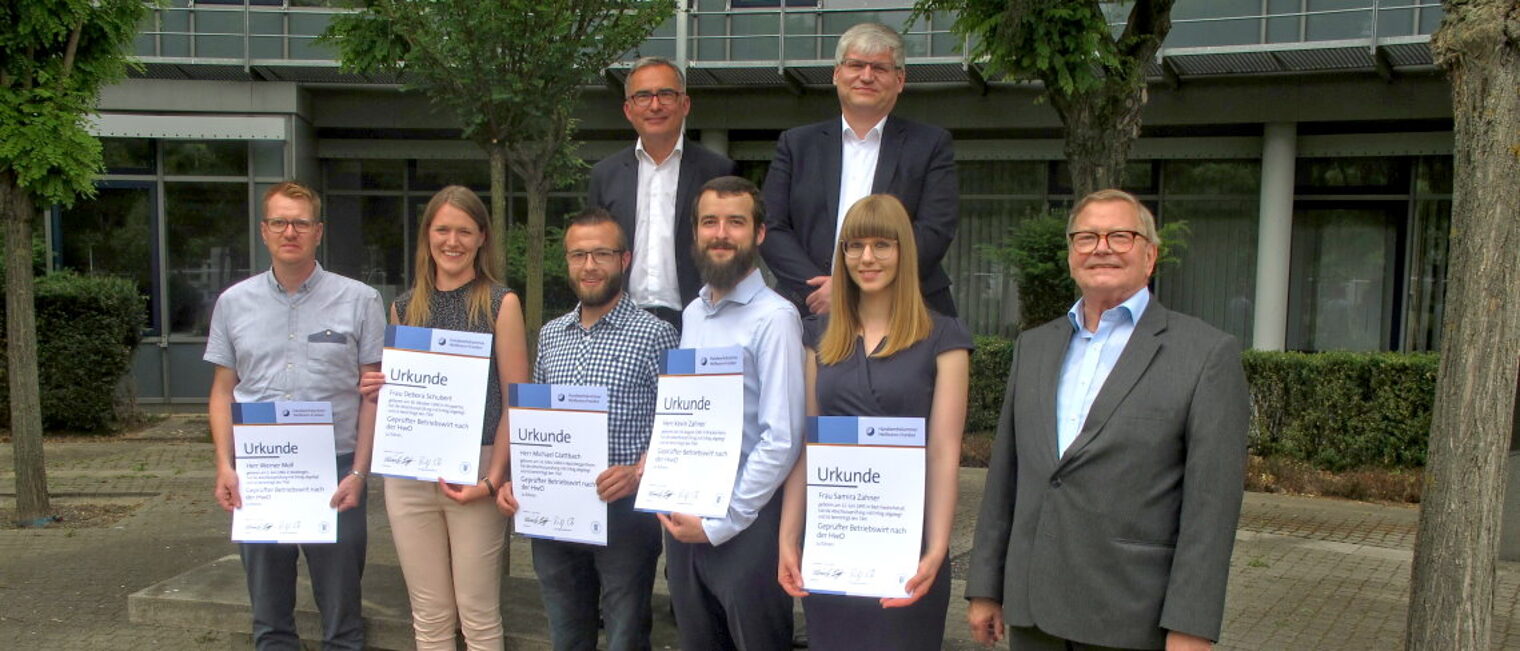 Erfolgreicher Abschluss: die neuen Betriebswirte. Zwei Reihen mit insgesamt acht Personen. Fünf davon halten eine Urkunde in ihren Händen.