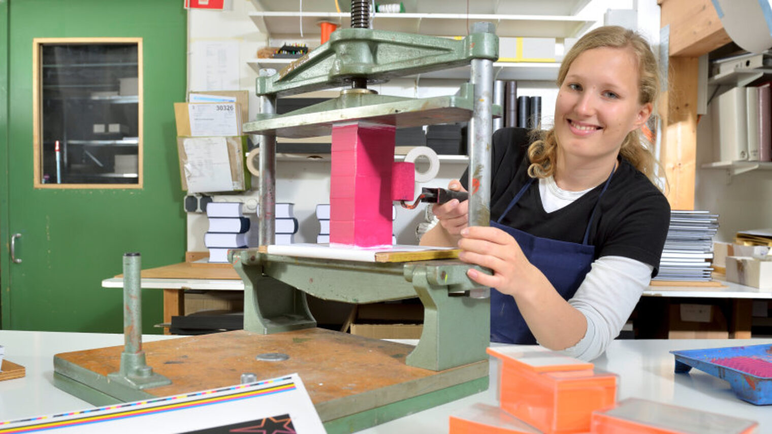 Werkstatt, Frau an Buchbindemaschine, Klebstoffbehälter