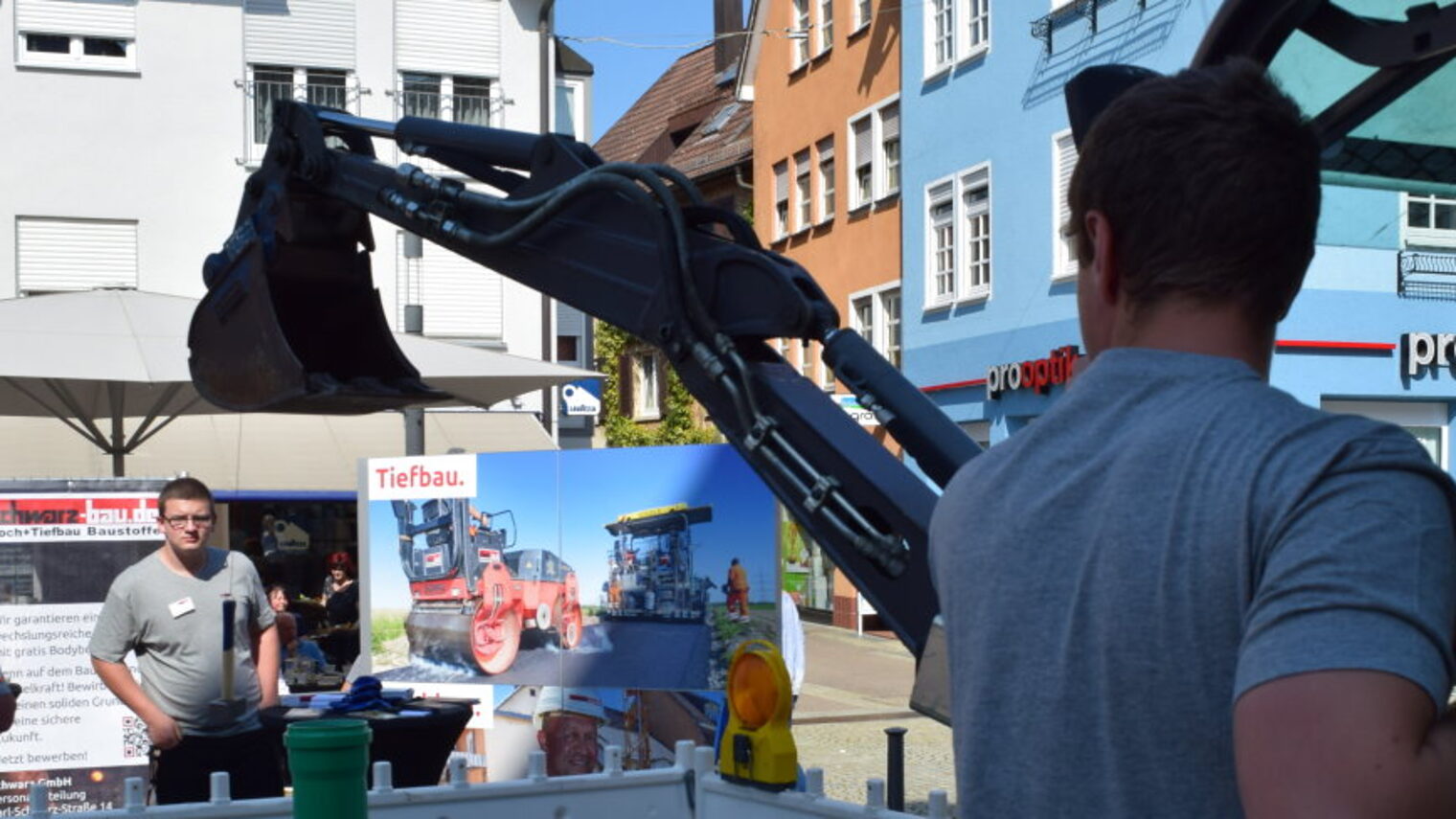 Ein Mann steht in einer Fußgängerzone an einem kleinen Bagger und erklärt interessierten Jugendlichen, wie er funktioniert.