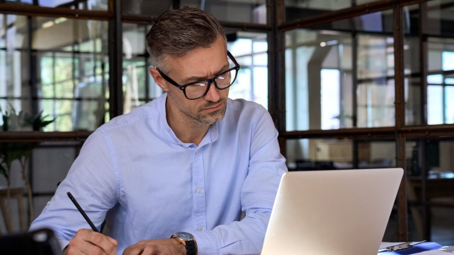 Ein Geschäftsmann sitzt im Büro am Laptop und nimmt an einem Web-Seminar teil, er macht sich Notizen.