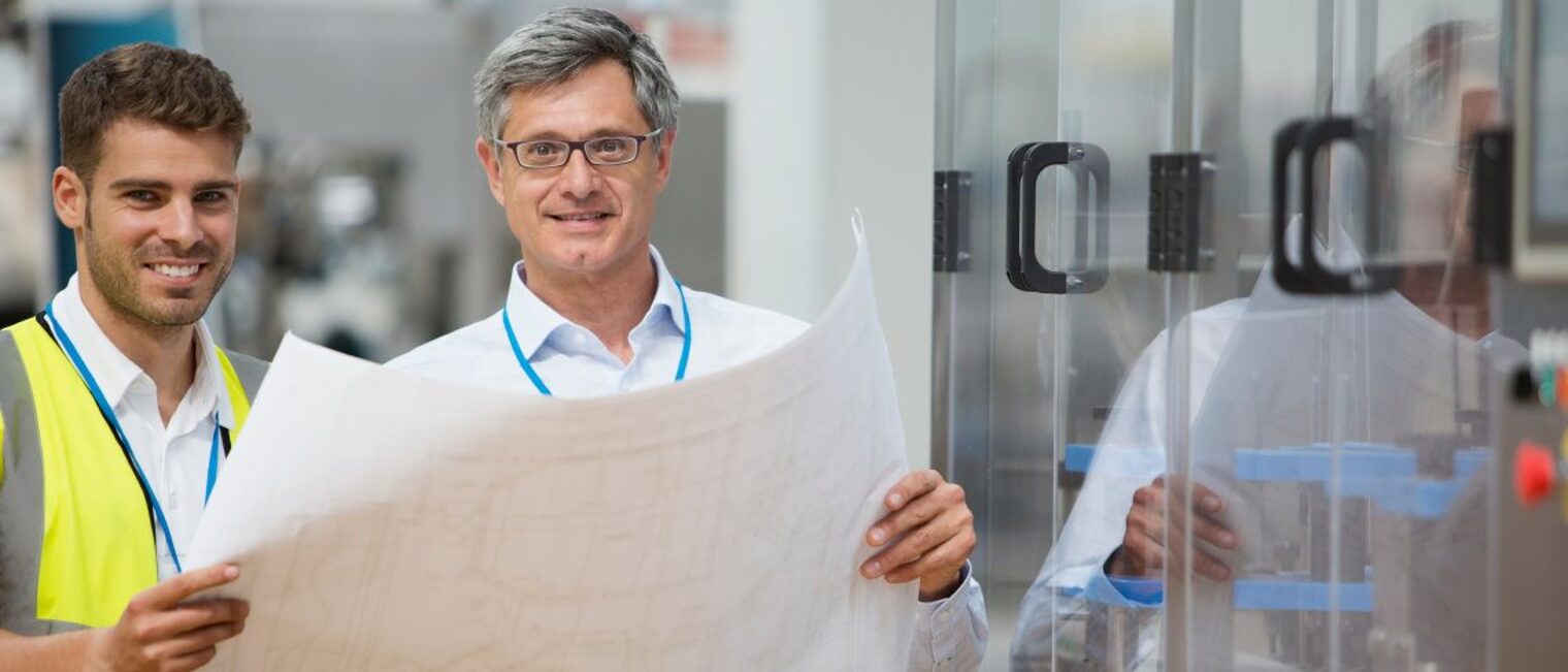 Der Seifriz-Preis prämiert gemeinsame Projekte von Handwerk und Wissenschaft. Zwei Männer halten gemeinsam einen Plan und lächeln in die Kamera.