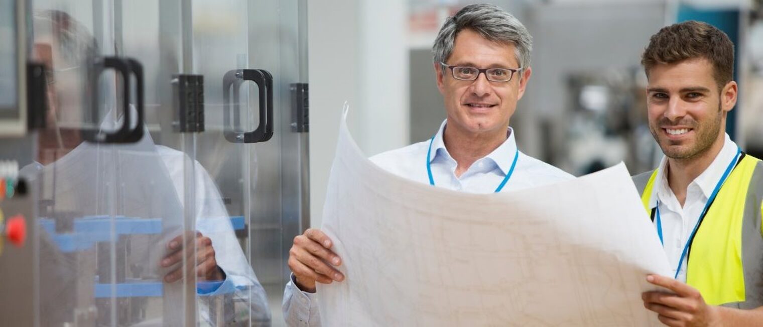 Der Seifriz-Preis prämiert gemeinsame Projekte von Handwerk und Wissenschaft. Zwei Männer halten gemeinsam einen Plan und lächeln in die Kamera.