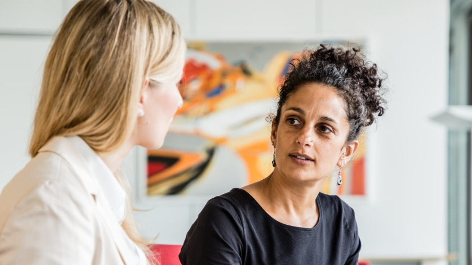 zwei Frauen sitzen am Besprechungstisch und unterhalten sich, sie schauen sich an.