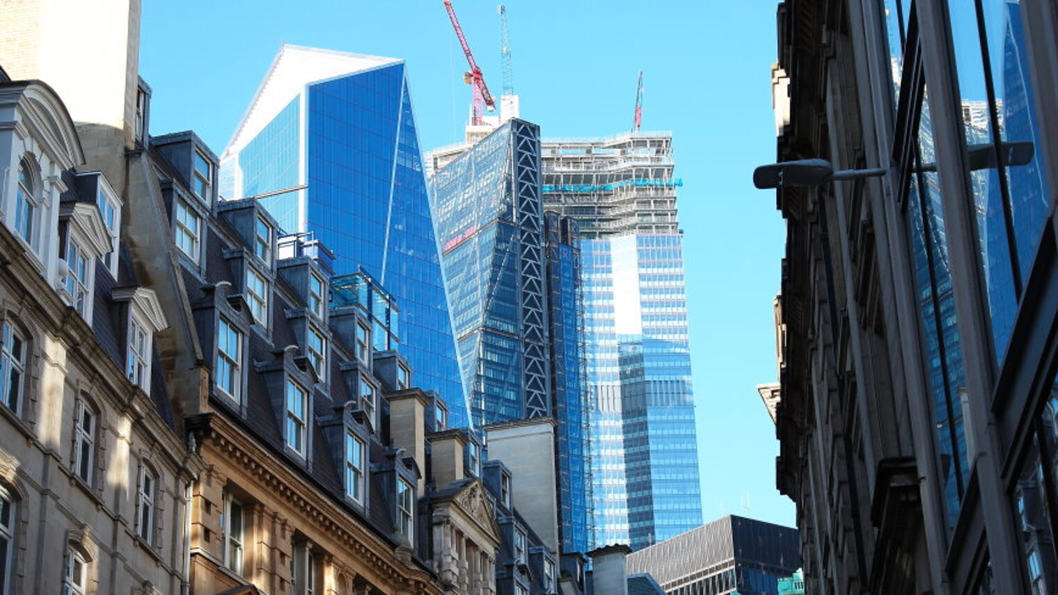 In den Straßen von London sieht man historische und moderne Gebäude, im Hintergrund gibt es Wolkenkratzer mit Baukränen.