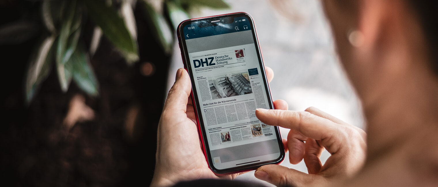 Eine Frau hält ein Smartphone in der Hand. Auf dessen Display ist die App der Deutschen Handwerks Zeitung zu sehen. 