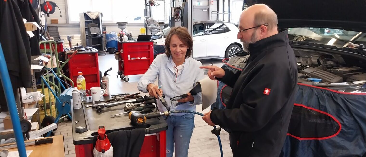 Eine Frau und ein Mann stehen in einer Autowerkstatt, die Frau hat ein Messerät in der Hand.