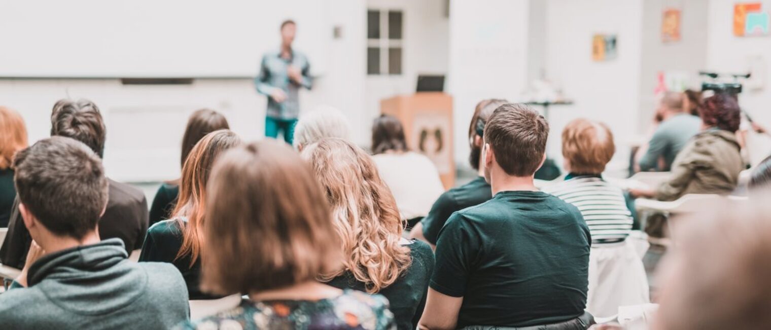 Seminare für Ehrenamtliche im Handwerk starten im November. Mehrere Frauen und Männer sitzen in einem großen Raum und hören einem Referenten zu.