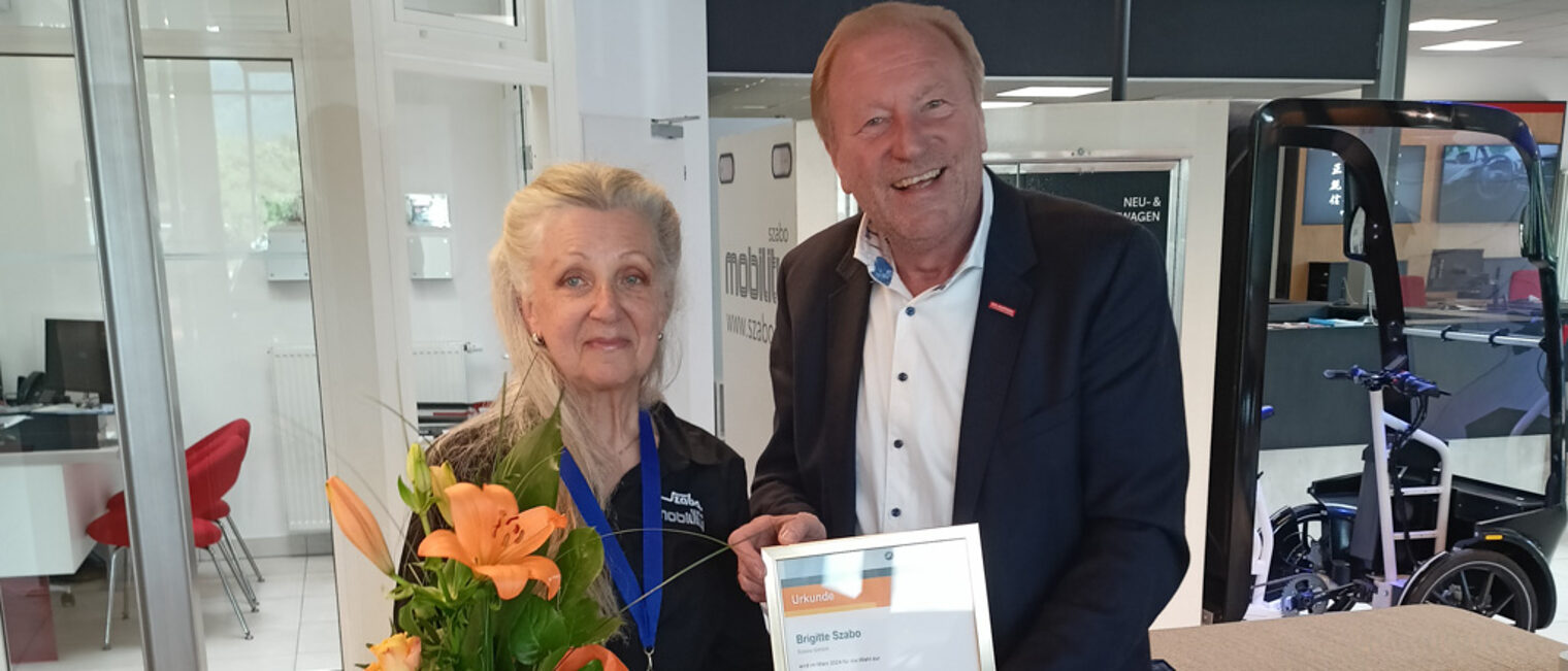 Ulrich Bopp überreicht Brigitte Szabo eine Auszeichnung mit Urkunde und einem Blumenstrauß