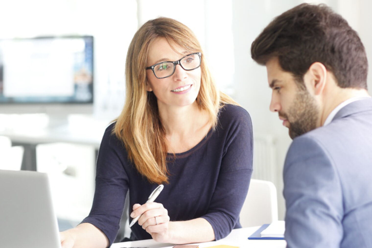 Eine Frau und ein Mann sitzen am Besprechungstisch, sie zeigt ihm etwas am Laptop.