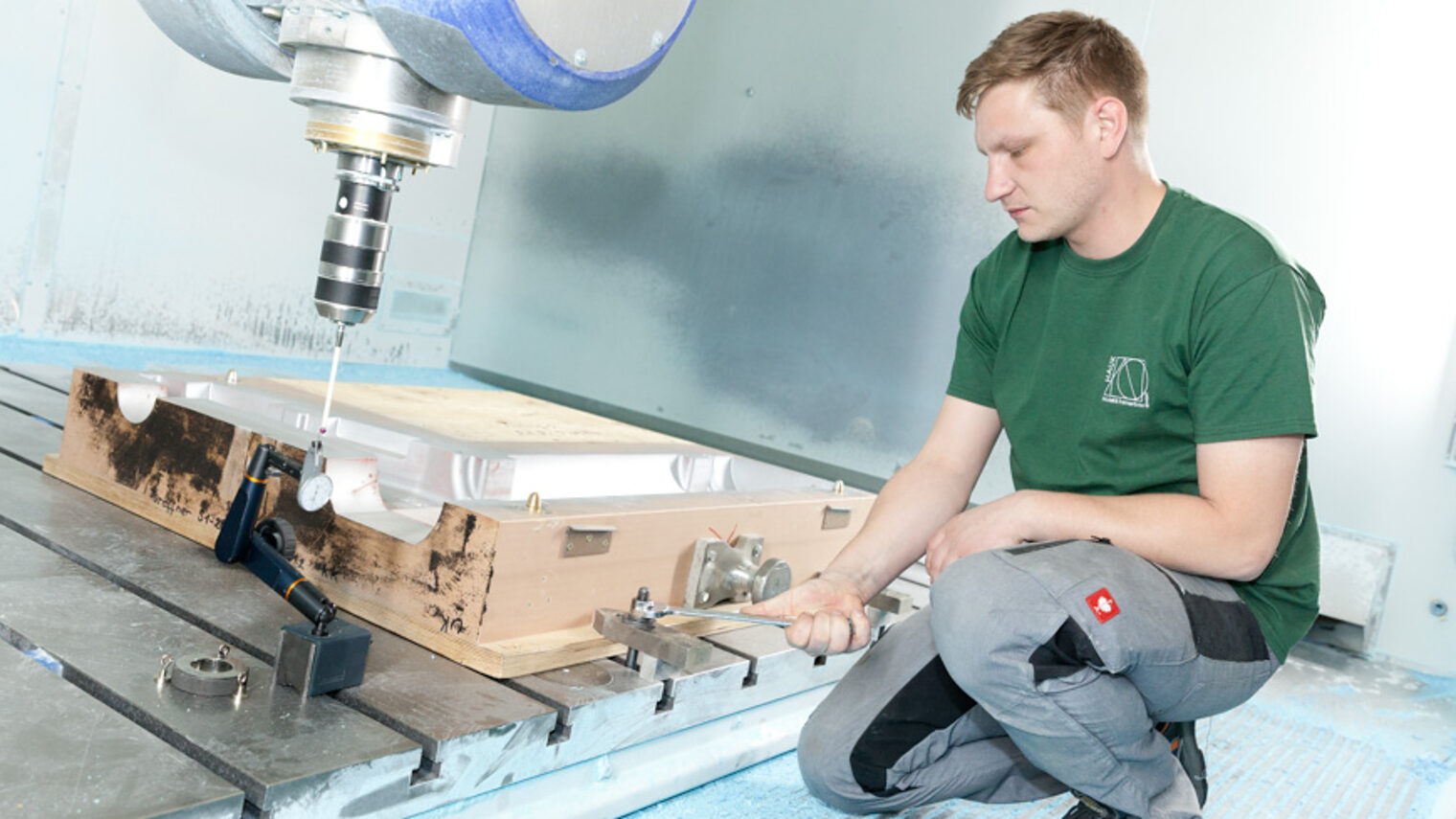 Ein Mann in Arbeitskleidung hockt neben einem Bauteil mit einem Schraubenschlüssel in der Hand. 
