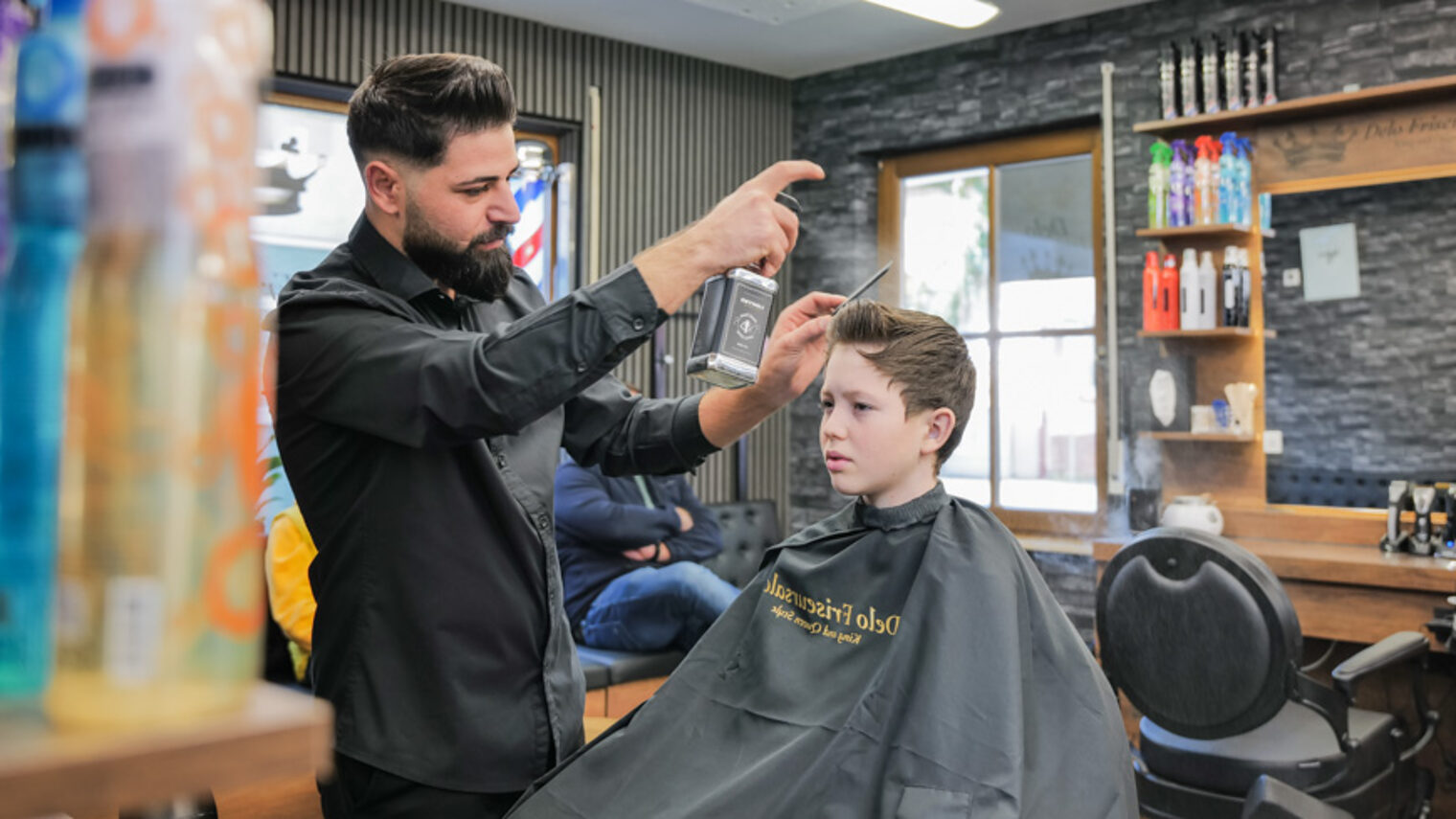 Ein Mann stylt in einem Friseursalon einem Jungen die Haare. 
