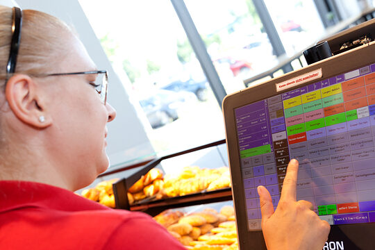 Eine Fachverkäuferin in einer Bäckerei tippt etwas in die Ladenkasse ein.