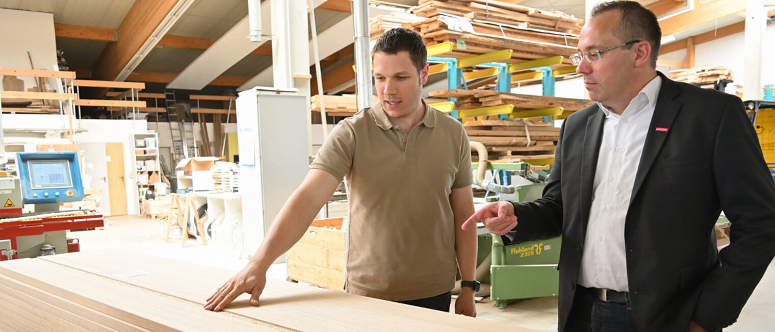 Die Mitarbeiter der Handwerkskammer begleiten Betriebe von der Gründung bis zur Nachfolge. Zwei Männer stehen in einer Schreinerwerkstatt und betrachten eine Holzplatte.