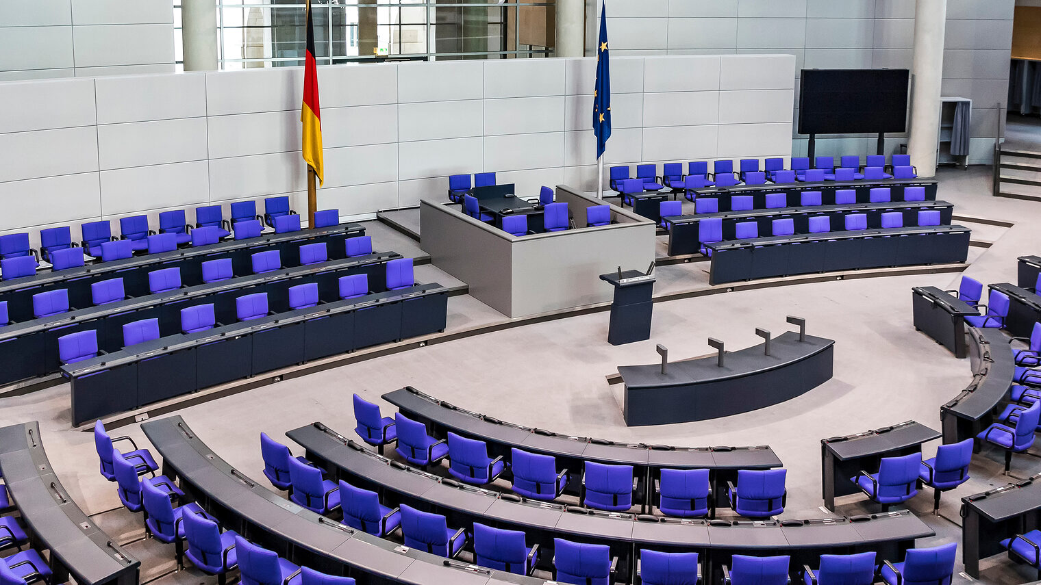 Der menschenleere Deutsche Bundestag mit der Deutschland- und Europa-Flagge im Hintergrund.