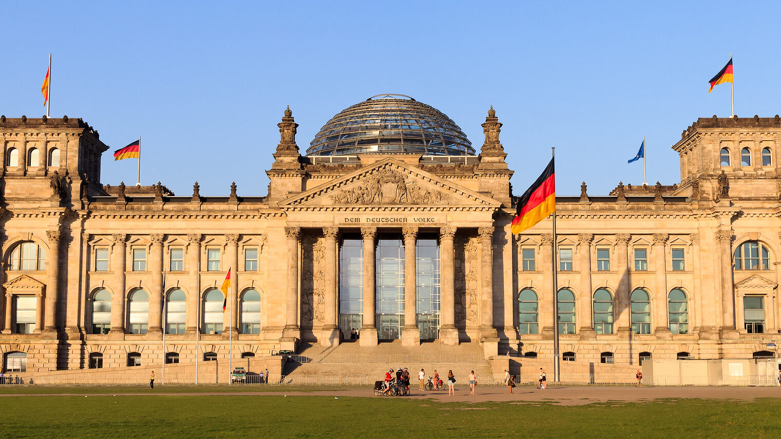 Frontalansicht des Deutschen Reichstags in Berlin mit Deutschlandfahnen und der berühmten Kuppel in der Mitte des Gebäudes.