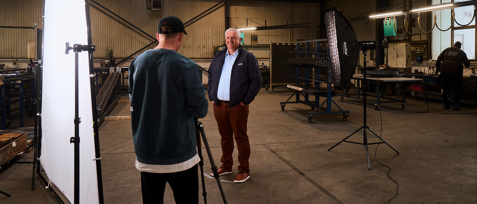 Mit seinem Betrieb ist Uwe Kraft Teil der Kampagne „mittel ist MEGA“. Ein Mann steht in einer Werkstatt und wird dort von einem Fotografen fotografiert.