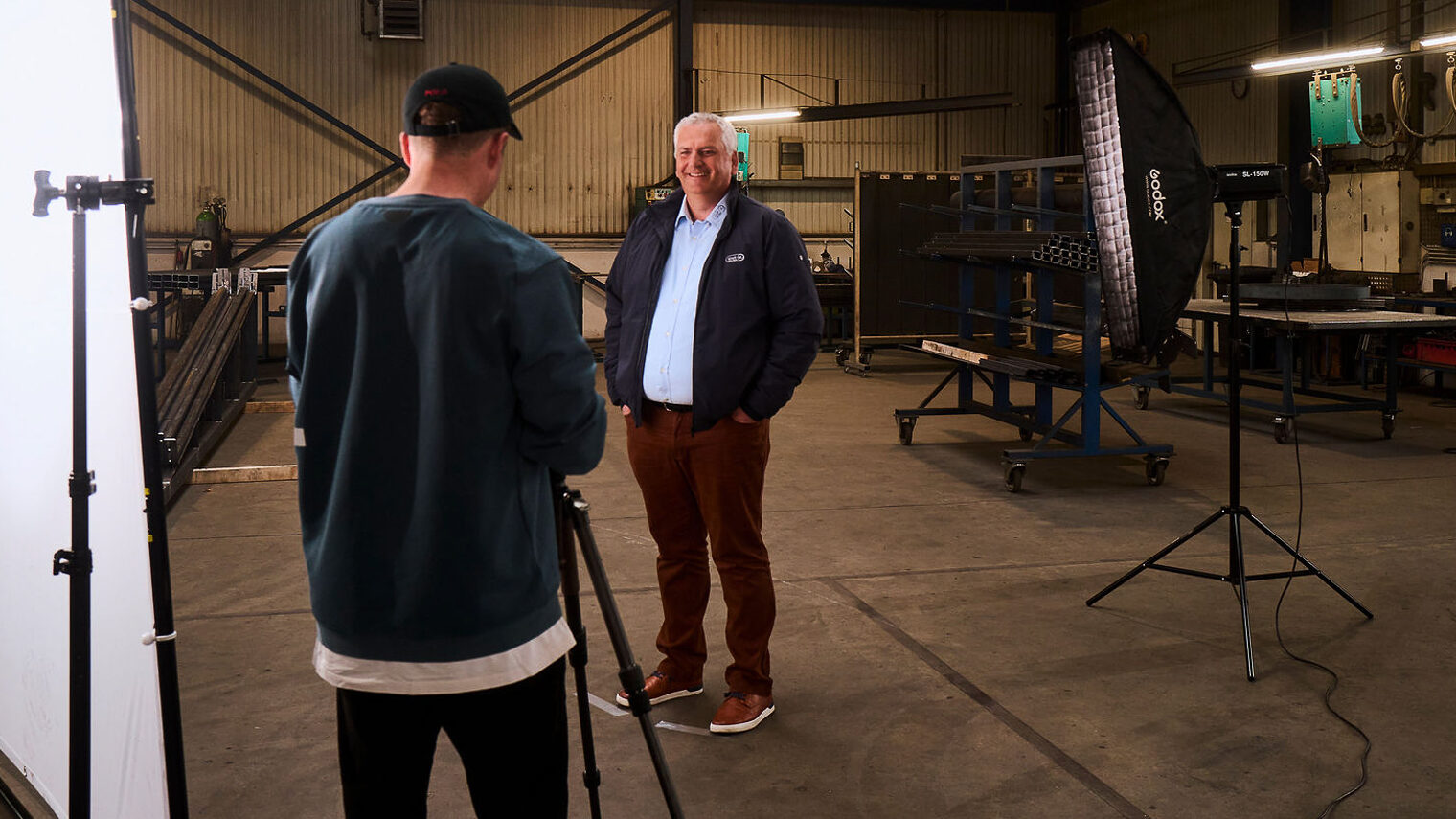 Ein Mann steht in einer Werkstatt und wird dort von einem Fotografen fotografiert.
