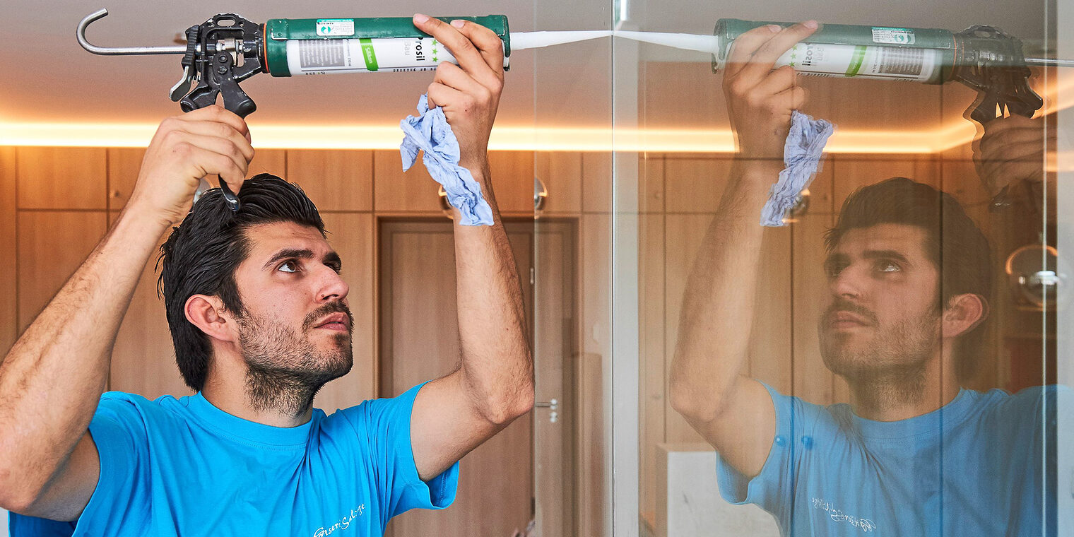 Ein Glaser dichtet die Fuge zwischen zwei Glasscheiben mit Silikon ab.