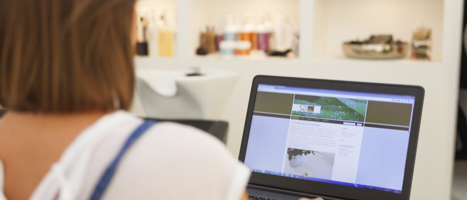 Vorgaben für Webseiten. In einem Friseursalon steht eine Frau an einem Laptop.