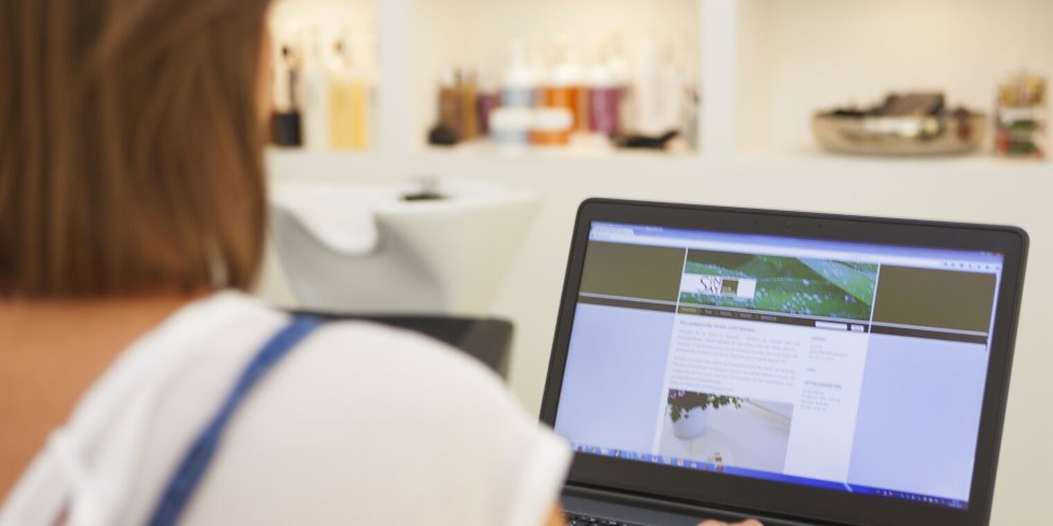 In einem Friseursalon steht eine Frau an einem Laptop.