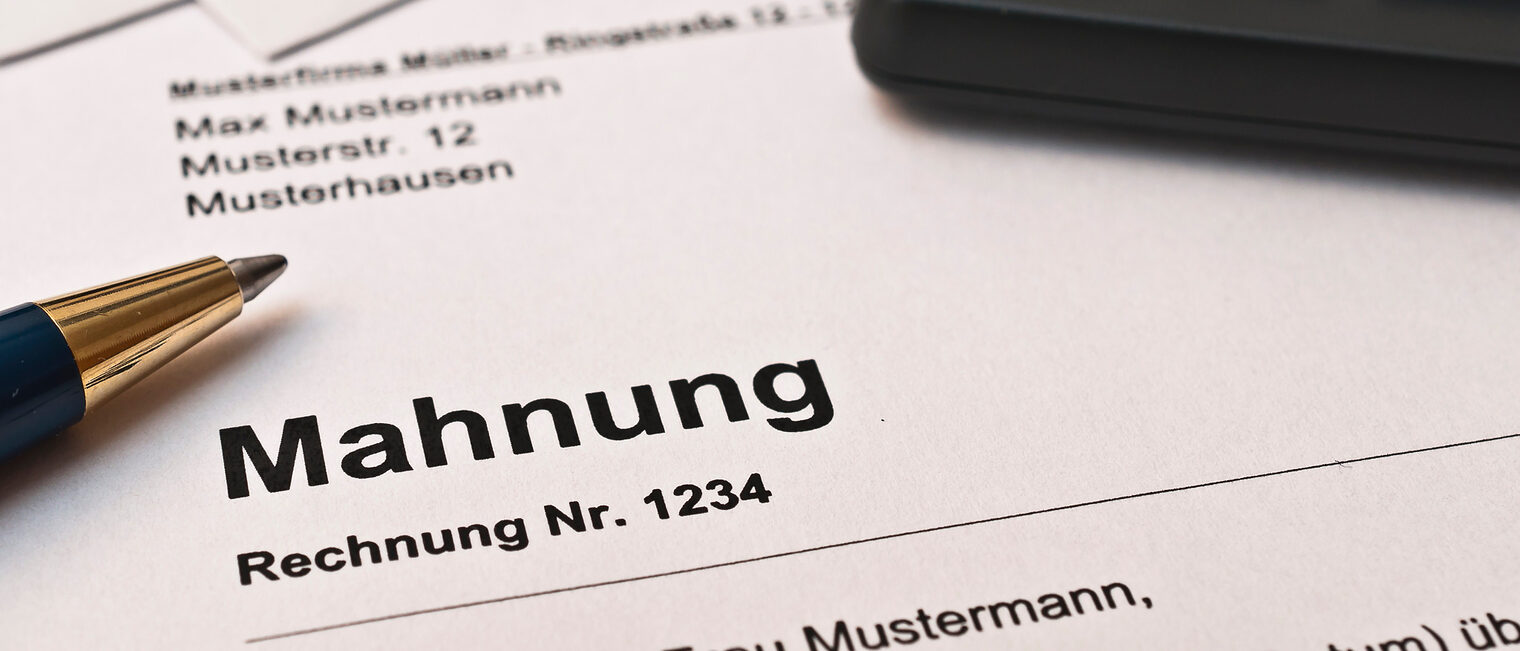 Unbezahlte Rechnungen können Handwerksbetriebe schnell in finanzielle Schwierigkeiten bringen. Ein Stift und ein Taschenrechner liegen auf einer Mahnung.