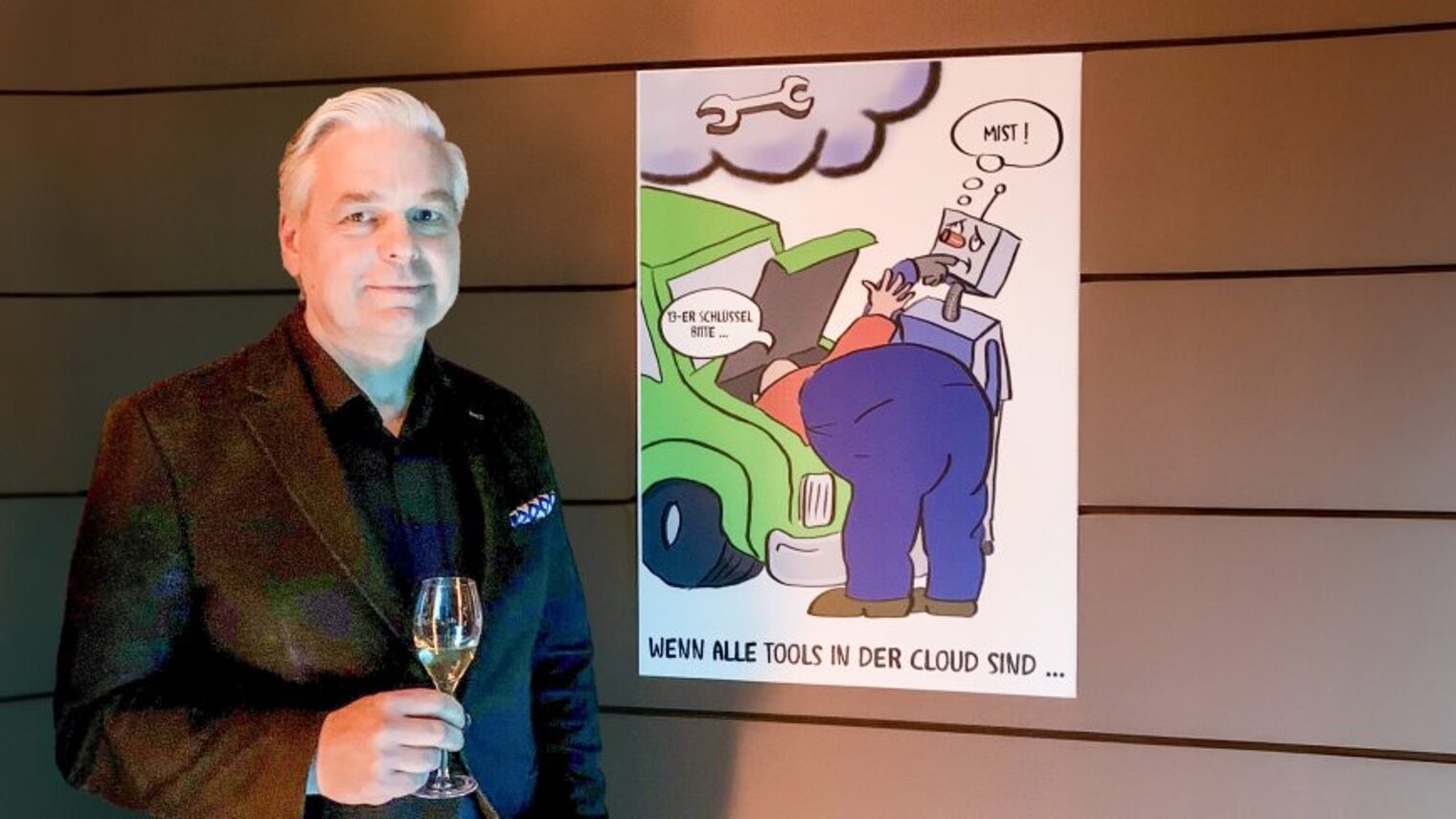 Ein Mann steht mit einem Sektglas vor einer Karikatur. 