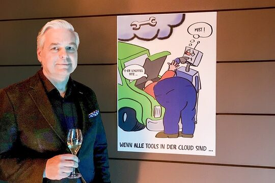 Ein Mann steht mit einem Sektglas vor einer Karikatur. 