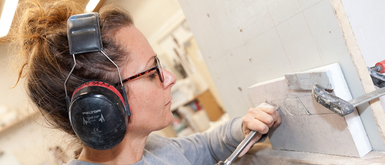 Frauen spielen in vielen Handwerksbetrieben eine wichtige Rolle. Eine Steinmetzin graviert einen Stein.