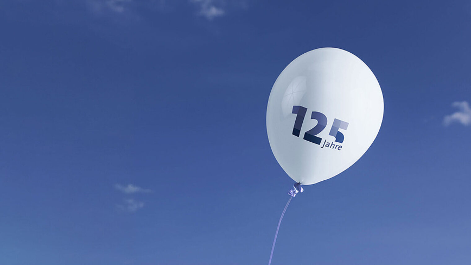 Ein weißer Luftballon mit der blauen Aufschrift "125 Jahre" schwebt rechts im Bild. Im Hintergrund ist der Himmel.
