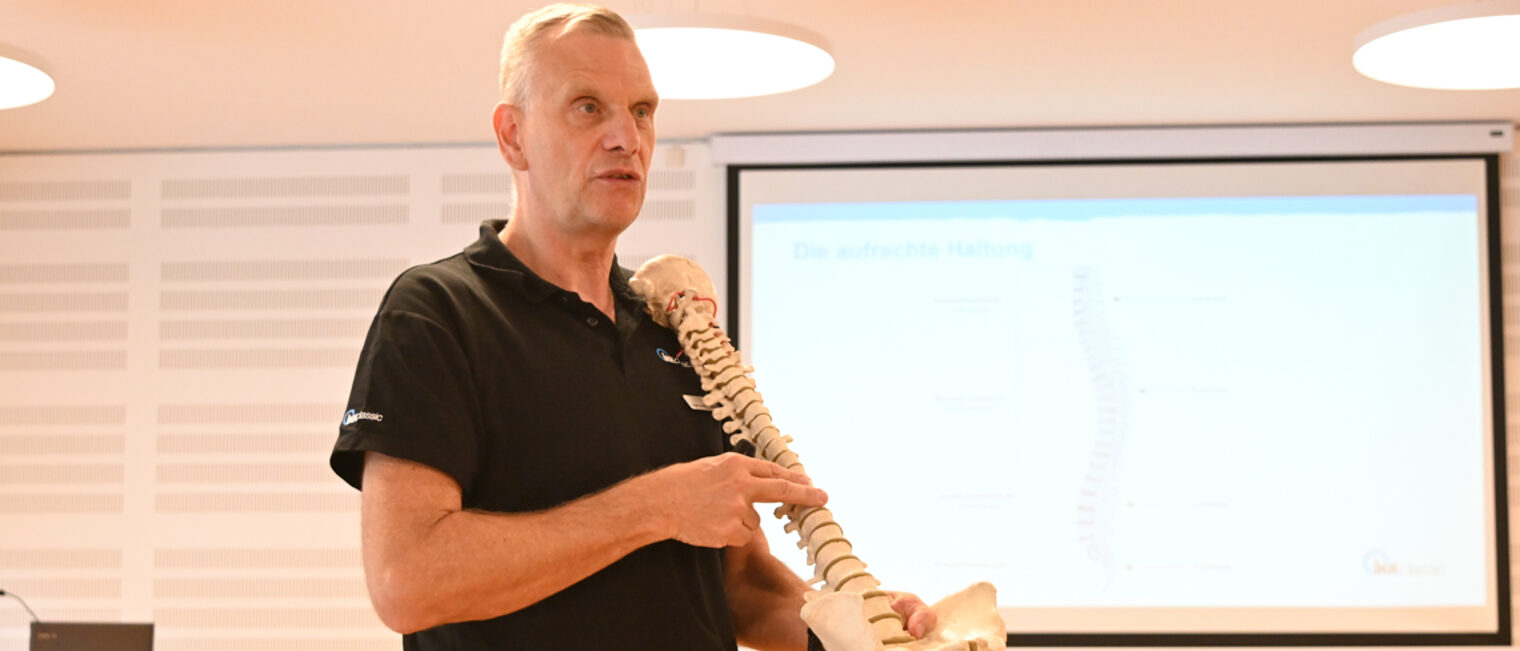 Jürgen Vorsatz von der IKK classic beim Gesundheitstag der Handwerkskammer. Ein Mann hält ein Wirbelsäulenskelett in der Hand.