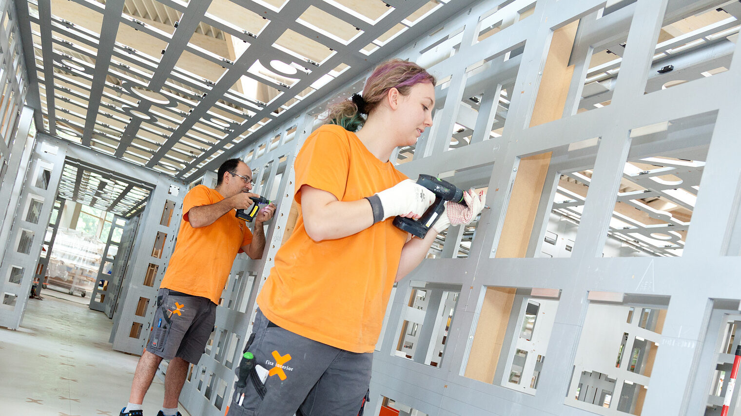 Eine Tischlerin und ein Tischler arbeiten zusammen mit Holz und Bohrmaschine