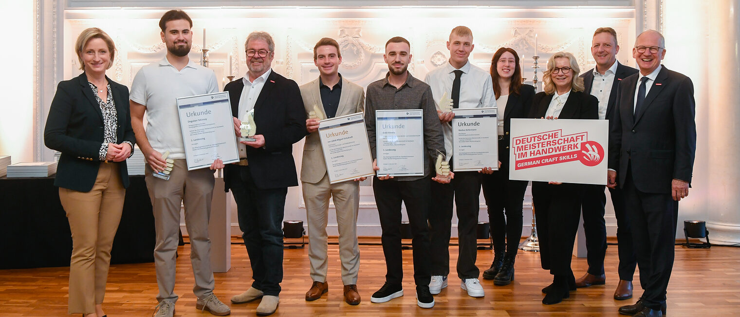 Im Rahmen einer Auszeichnung stehen mehrere Personen für ein Gruppenfoto nebeneinander und lächeln in die Kamera.