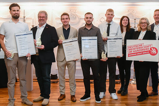 Im Rahmen einer Auszeichnung stehen mehrere Personen für ein Gruppenfoto nebeneinander und lächeln in die Kamera.