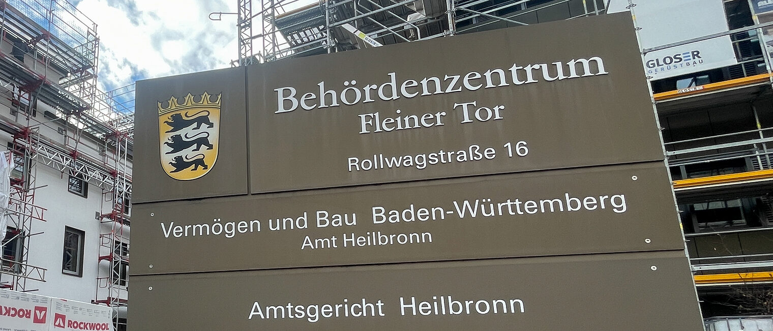 Vor einem Gebäude steht ein Schild. Auf dem Schild steht Behördenzentrum und Amtsgericht Heilbronn.
