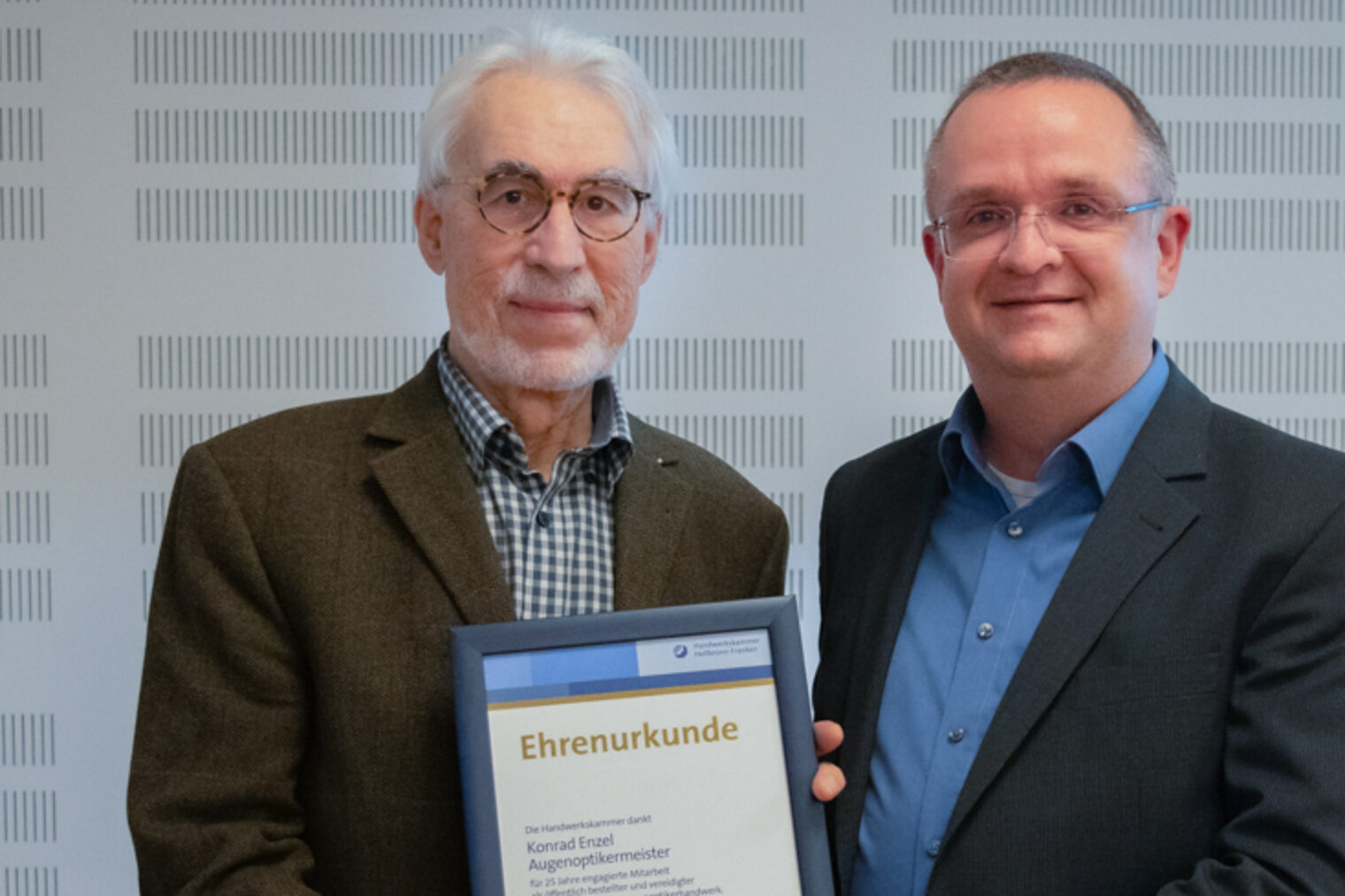 Zwei Männer halten eine Urkunde und lächeln in die Kamera.