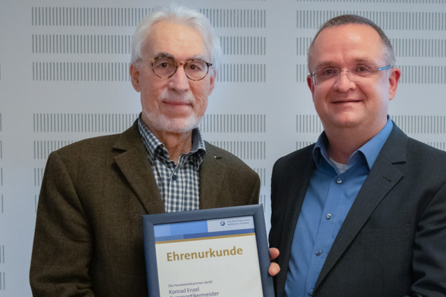 Zwei Männer halten eine Urkunde und lächeln in die Kamera.