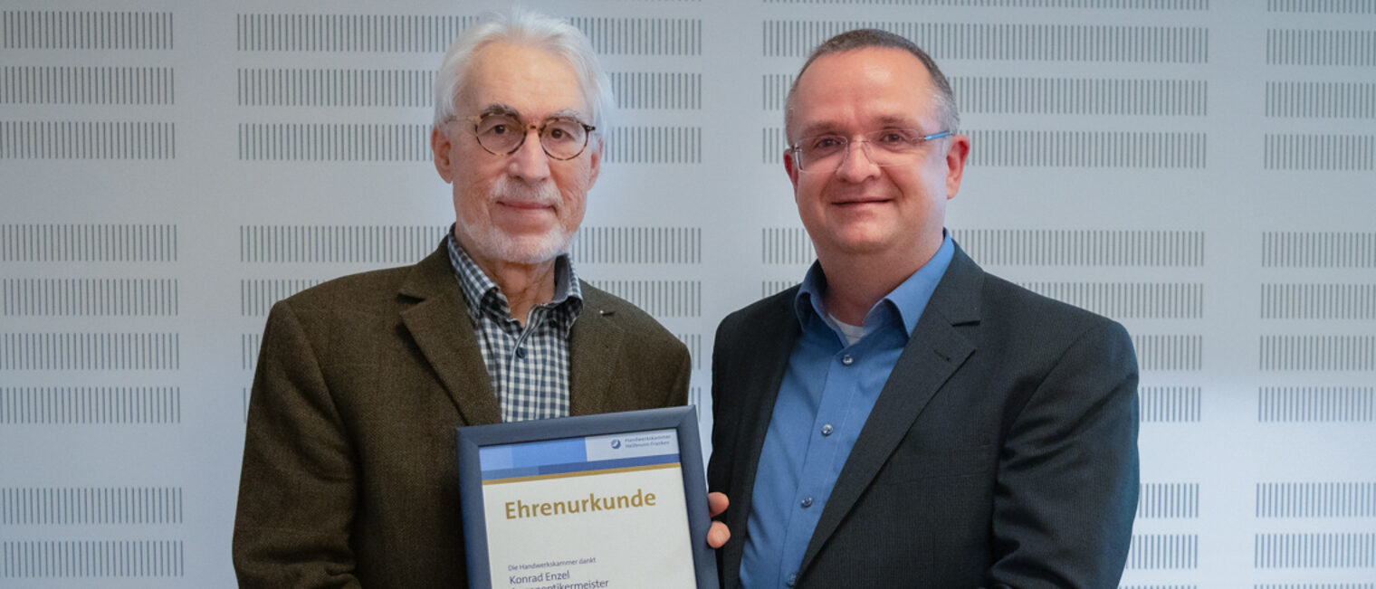 Zwei Männer halten eine Urkunde und lächeln in die Kamera.