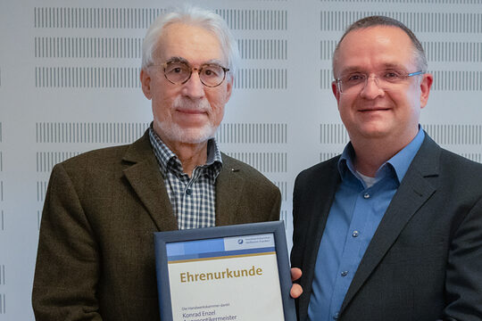 Zwei Männer halten eine Urkunde und lächeln in die Kamera.