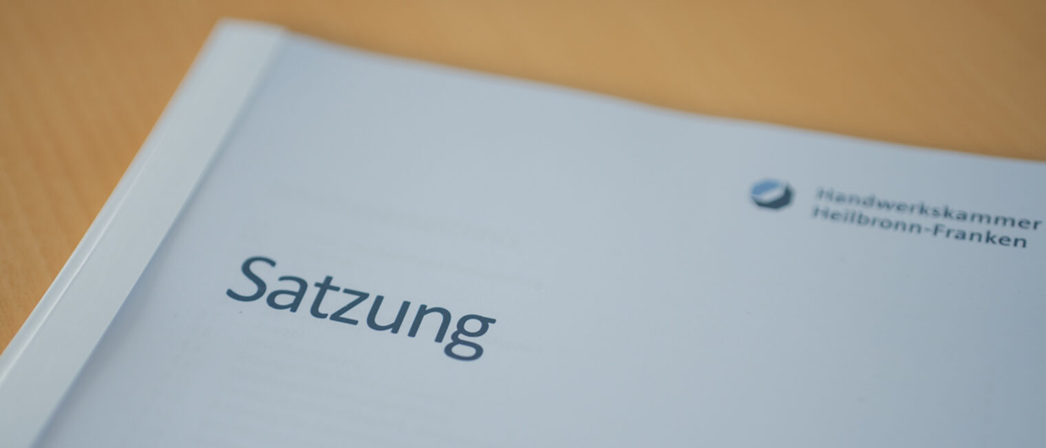 Auf einem Holztisch liegt ein Dokument mit dem Titel Satzung. 