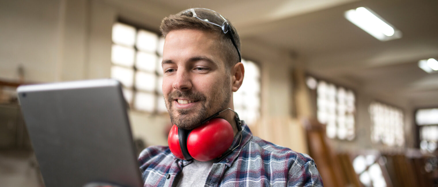 Ein Mann steht in einer Werkstatt und blickt auf ein Tablet.