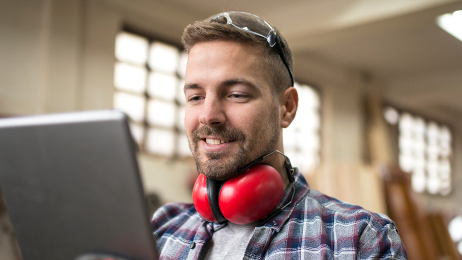 Ein Mann steht in einer Werkstatt und blickt auf ein Tablet.