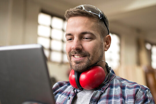 Ein Mann steht in einer Werkstatt und blickt auf ein Tablet.