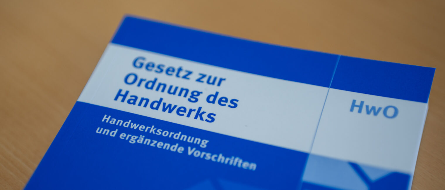 Ein blaues Buch mit dem Titel "Gesetz zur Ordnung des Handwerks" liegt auf einem Tisch.