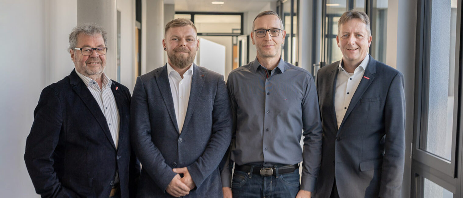 Vier Männer stehen in einer Reihe in einem Flur. 