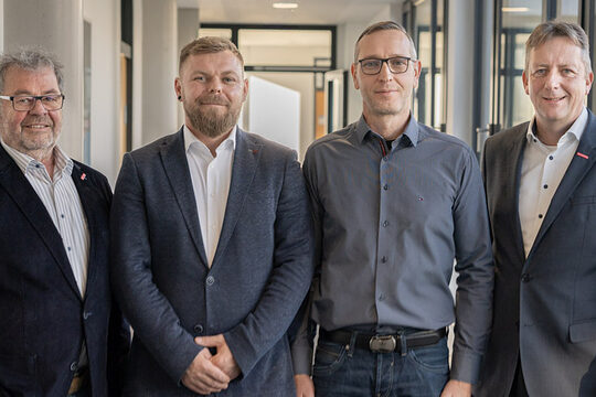 Vier Männer stehen in einer Reihe in einem Flur. 