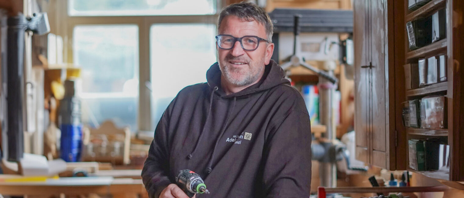 Ein Mann steht in einer Schreinerwerkstatt und hält einen Akku-Schreiber in der Hand. 