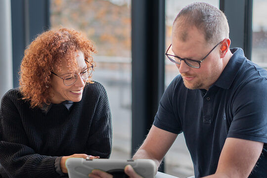 Eine Frau und ein Mann sitzen an einem Tisch und schauen gemeinsam auf ein Tablet.