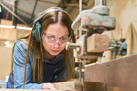Eine Auszubildende zur Schreinerin steht an einer Werkbank und schneidet ein Stück Holz zurecht.