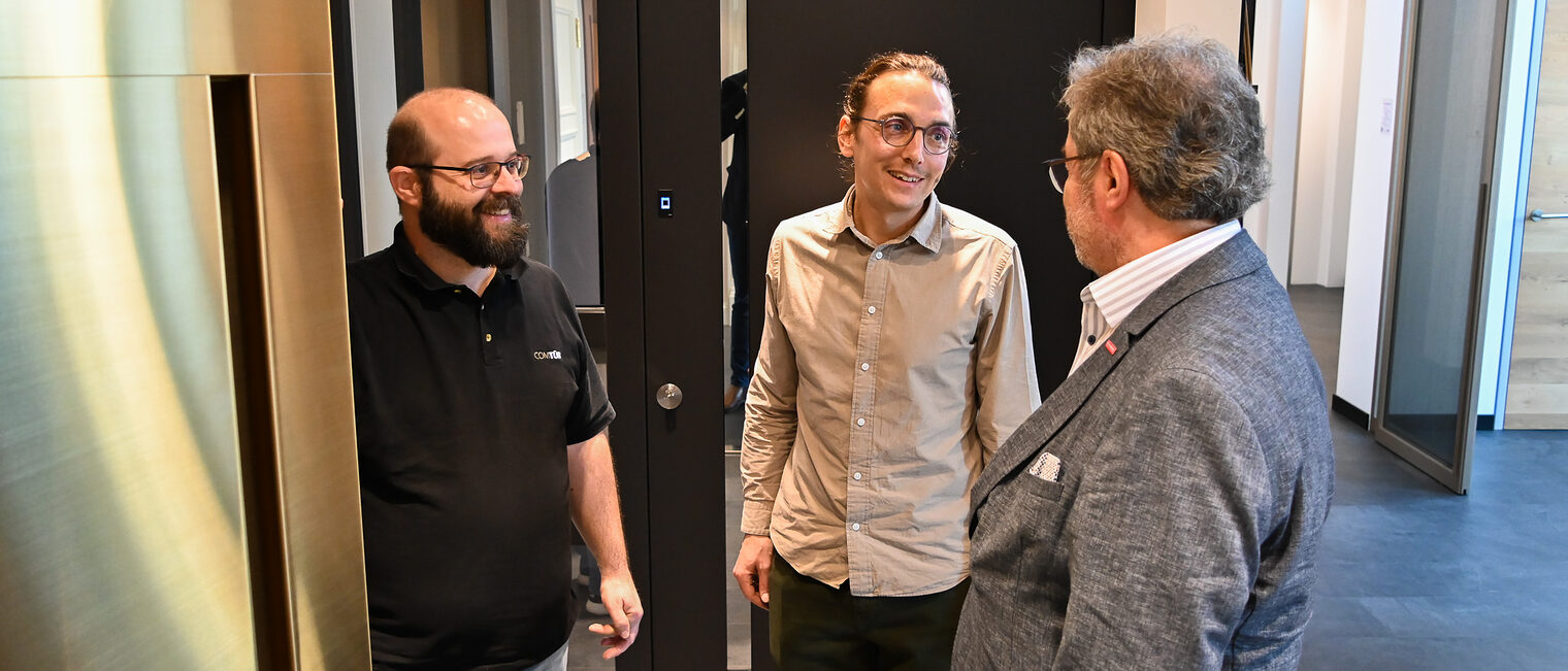 In einem Ausstellungsraum schauen sich drei Männer verschiedene Türmodelle an und unterhalten sich dabei.